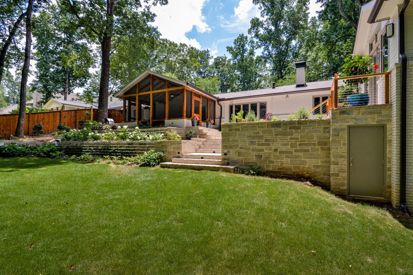 Backyard with lawn, stone retaining wall and house beyond in a Sandy Springs home